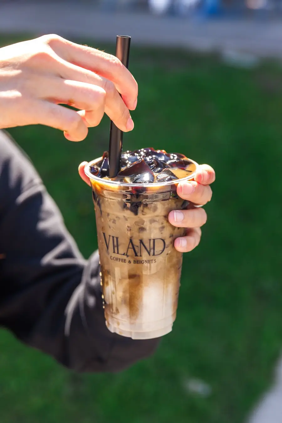 A ViLand iced drink topped with grass jelly, held outdoors.